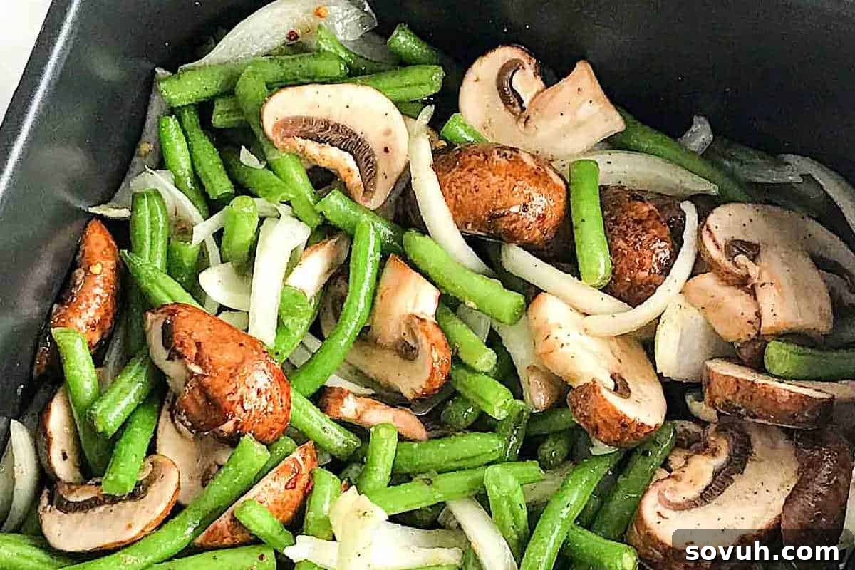 green beans, mushrooms, and onion tossed together in an air fryer