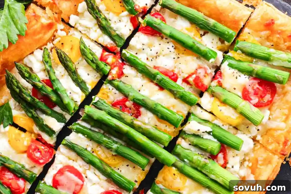 Close-up of a sliced vegetable pizza topped with asparagus, tomatoes, and cheese.