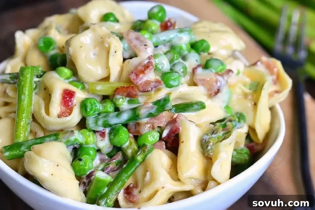 A bowl of creamy pasta with green peas, asparagus, and bacon pieces.