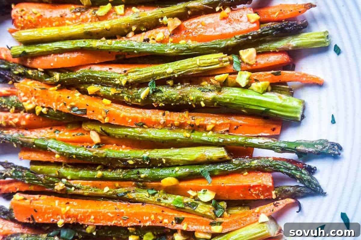Roasted carrots and asparagus garnished with chopped herbs and spices on a white plate.