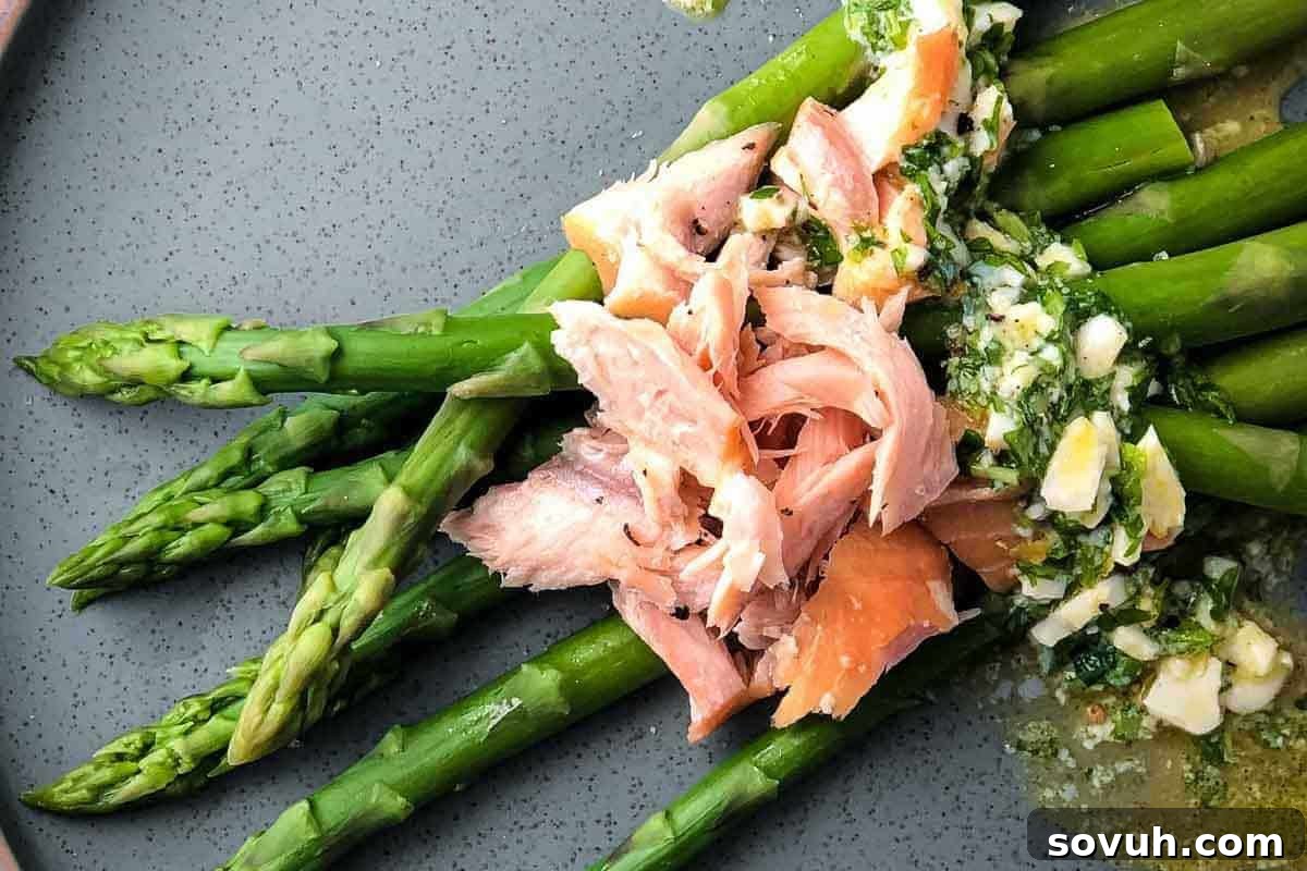 A plate of steamed asparagus topped with smoked salmon and garnished with chopped eggs and herbs.