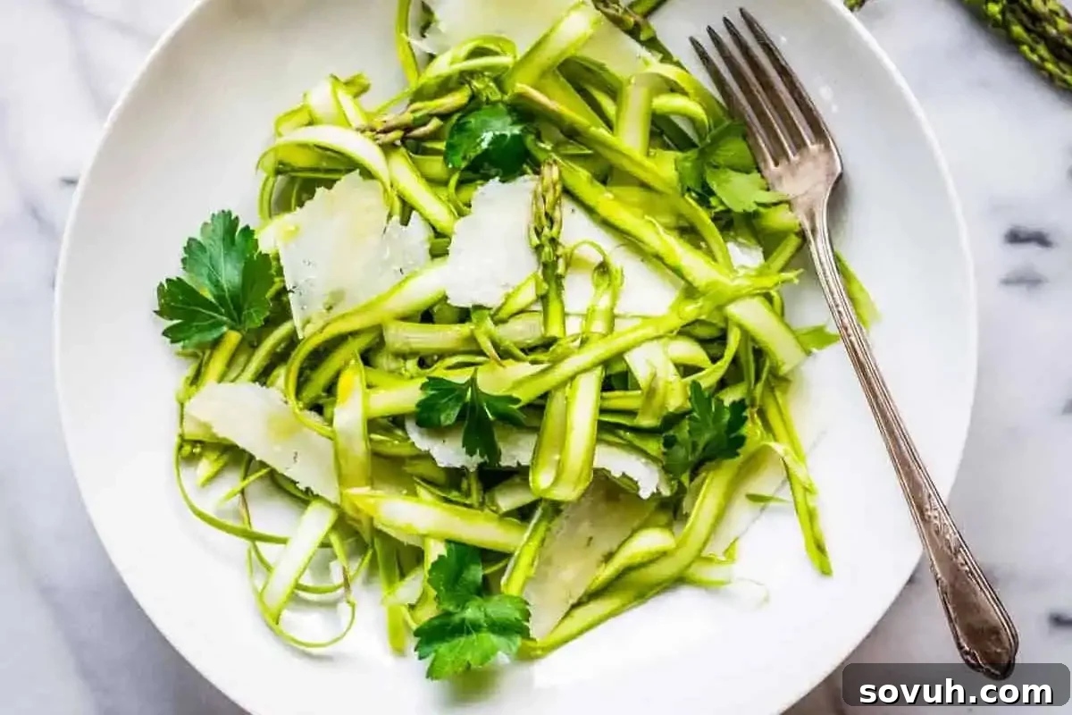 A fresh zucchini noodle salad with shaved cheese and parsley in a white bowl, served with a fork on a marble surface.