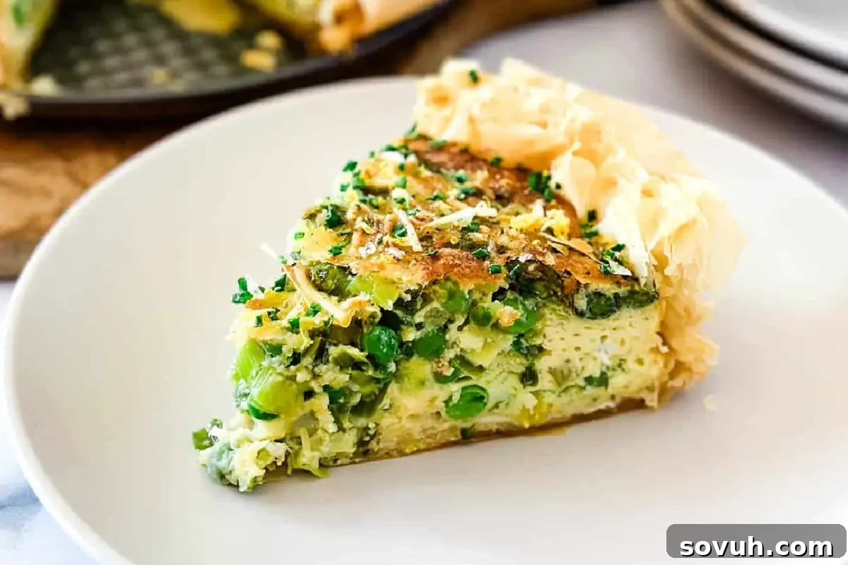A slice of savory pie with a flaky crust and green vegetable filling, garnished with chives, on a white plate.