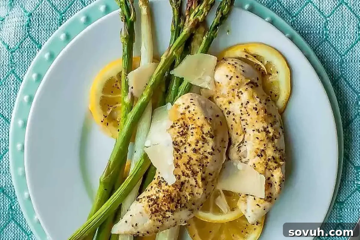 Grilled chicken breasts topped with slices of parmesan, served with roasted asparagus and lemon slices on a white plate.