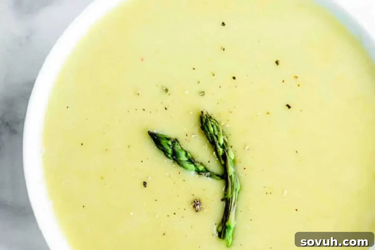A bowl of creamy asparagus soup garnished with two spears of asparagus and freshly ground black pepper.