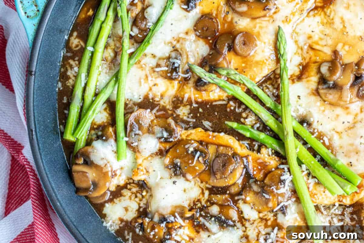Close-up of a skillet meal with melted cheese, sautéed mushrooms, and asparagus, sprinkled with grated parmesan.
