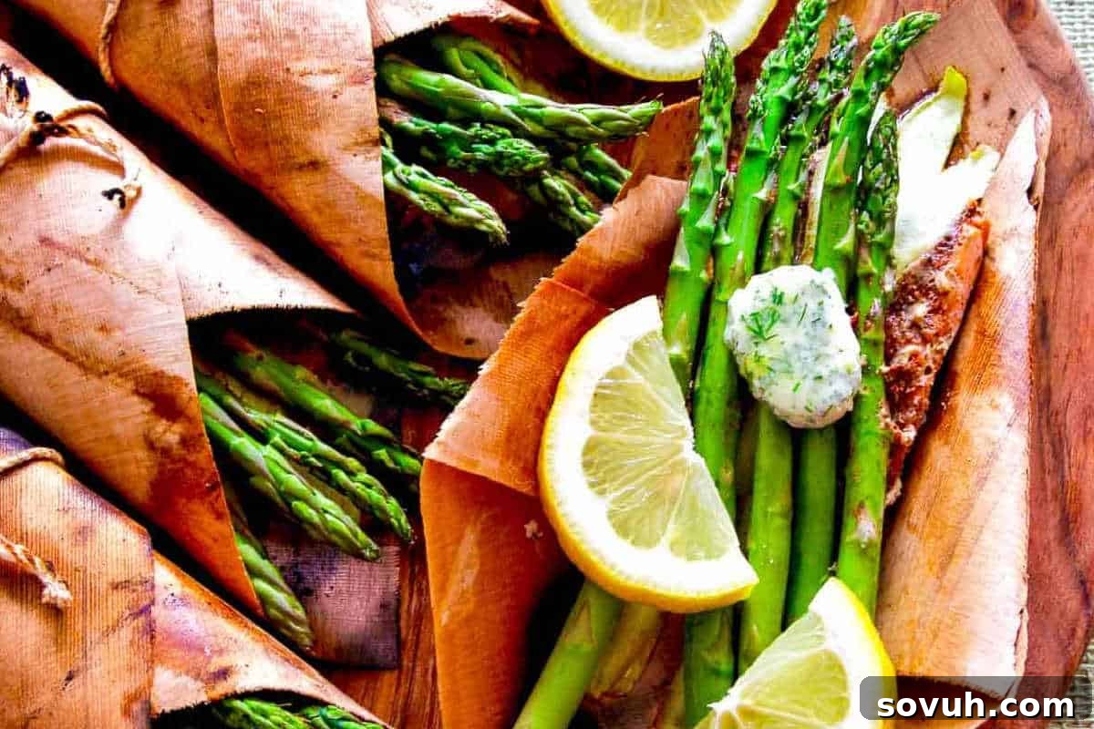 Cooked asparagus with lemon slices and herb butter served on a wooden board.