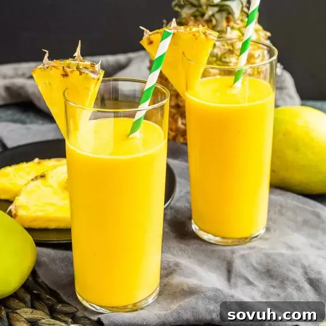 Two vibrant mango pineapple smoothies garnished with fresh pineapple wedges, ready to be enjoyed as a healthy and refreshing drink.