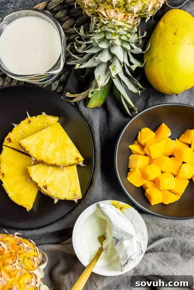 Fresh ingredients laid out for a mango pineapple smoothie: carefully diced ripe mango, bright pineapple chunks, a glass of almond milk, and a bowl of creamy Greek yogurt.