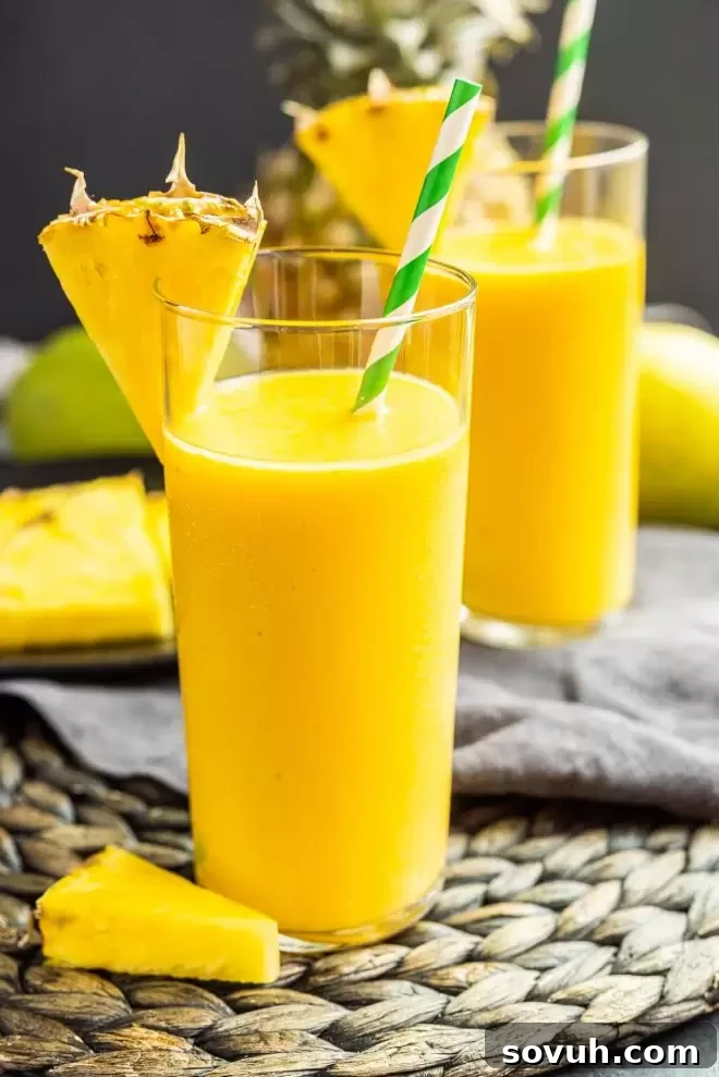A single mango pineapple smoothie glass, perfectly blended and garnished with a pineapple wedge, showcasing its creamy, golden texture ready for enjoyment.