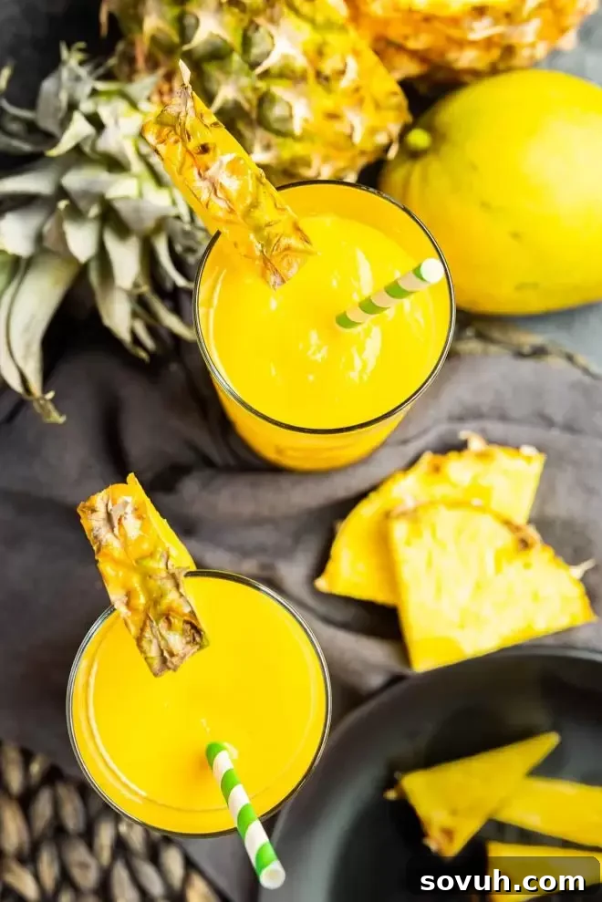 Two cheerful mango pineapple smoothies with colorful striped paper straws, presented invitingly for enjoyment.