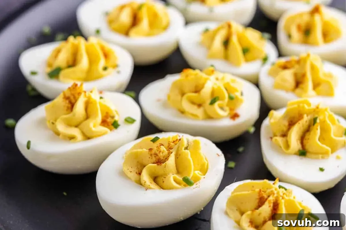 A plate of deviled eggs garnished with paprika and chopped chives, presented on a dark surface.