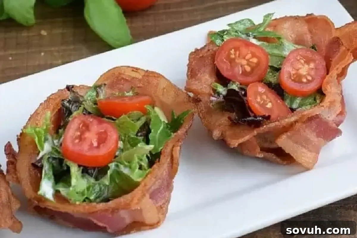 Two bacon cups filled with salad and topped with cherry tomato slices, presented on a white rectangular plate.