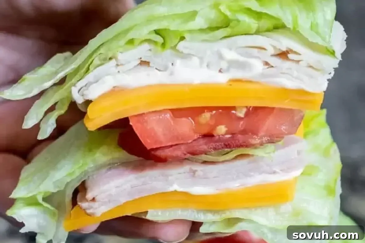 A hand holding a lettuce wrap filled with layers of turkey, cheese, and sliced tomatoes.