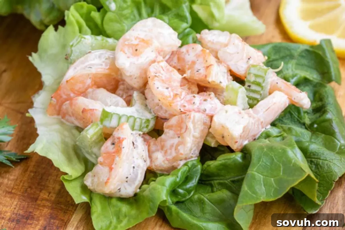 A low carb shrimp salad with celery and lemon on leafy greens, served on a wooden board.