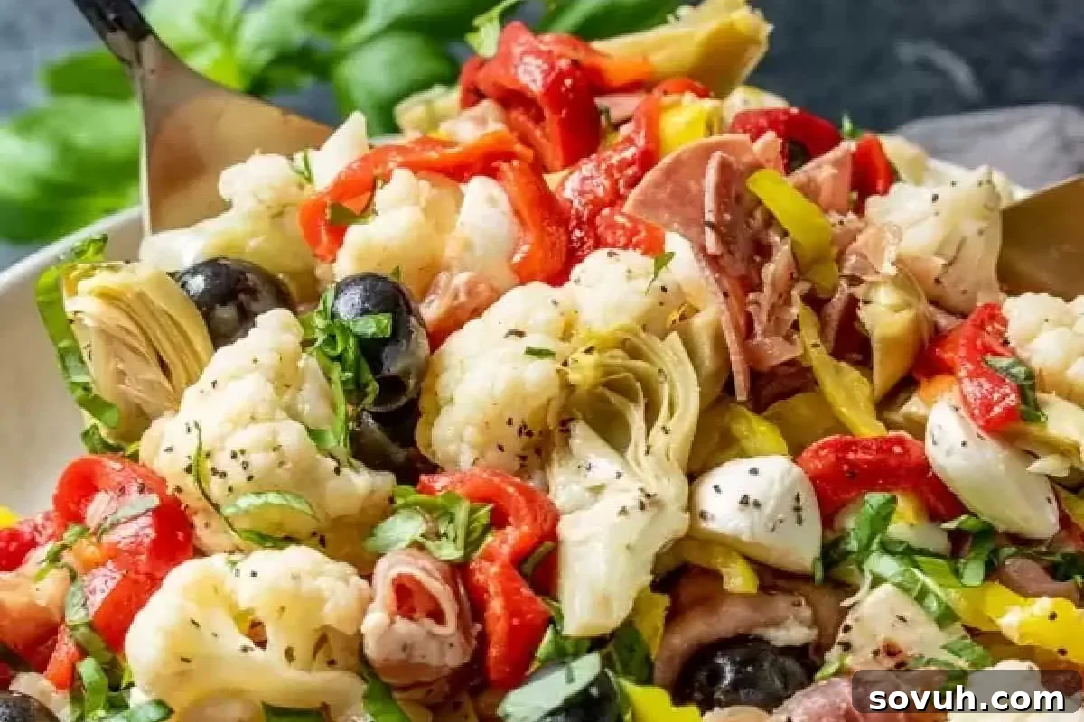 Close-up of a colorful antipasto salad with artichokes, olives, cured meats, cheese, and vegetables, served in a bowl with a fork.