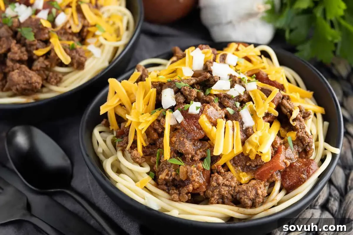 Two enticing bowls of authentic Cincinnati Chili, featuring spaghetti generously topped with unique chili, shredded cheddar cheese, and diced onions, served alongside crispy garlic bread.