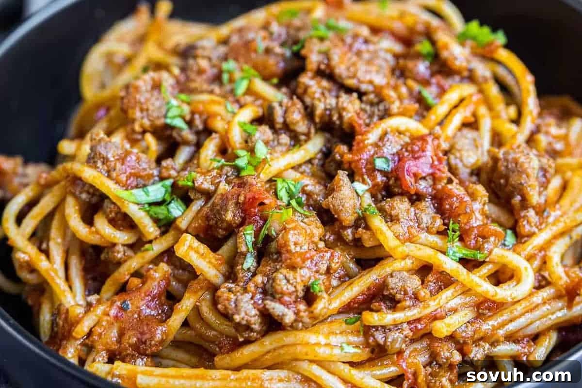 A close-up of perfectly cooked Instant Pot Spaghetti Bolognese, generously topped with a rich meat sauce and fresh chopped parsley, served in a sleek black bowl.