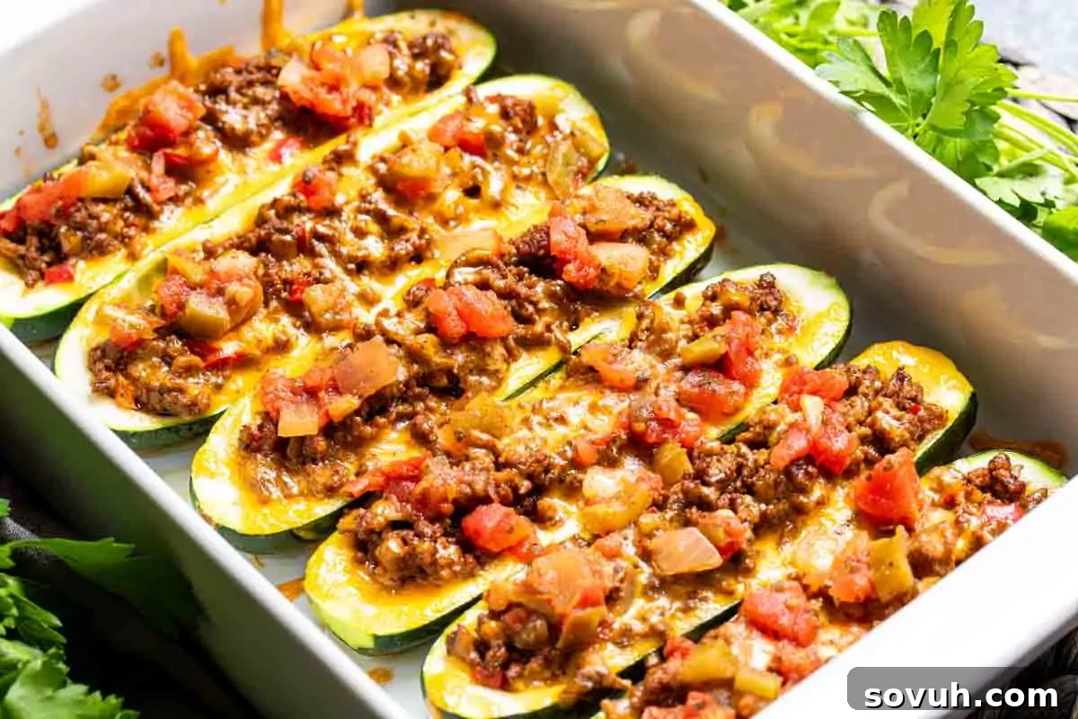 Healthy and flavorful Taco Stuffed Zucchini Boats, generously filled with seasoned ground beef, colorful bell peppers, melted cheese, and diced tomatoes, garnished with fresh parsley on a white plate.