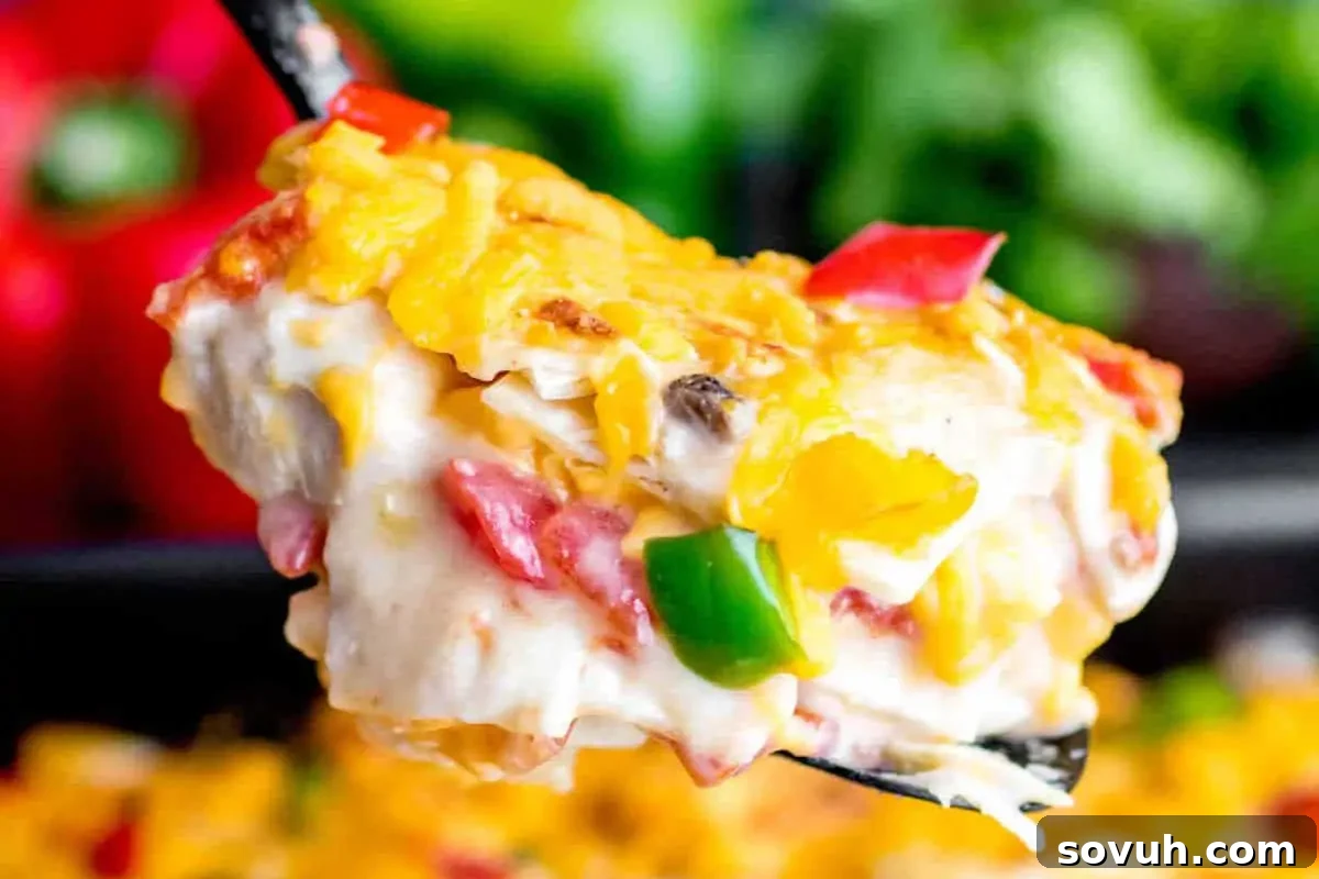 A close-up of a fork lifting a cheesy slice of vegetable casserole with visible pieces of green and red bell peppers.