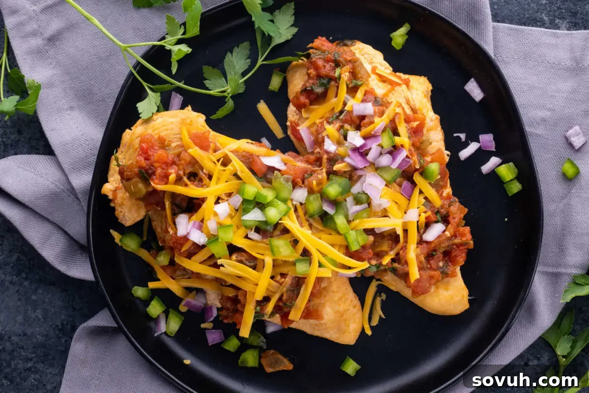 Two stuffed tacos topped with cheese, diced onions, and sliced green chili peppers, served on a black plate with fresh cilantro and a gray napkin.