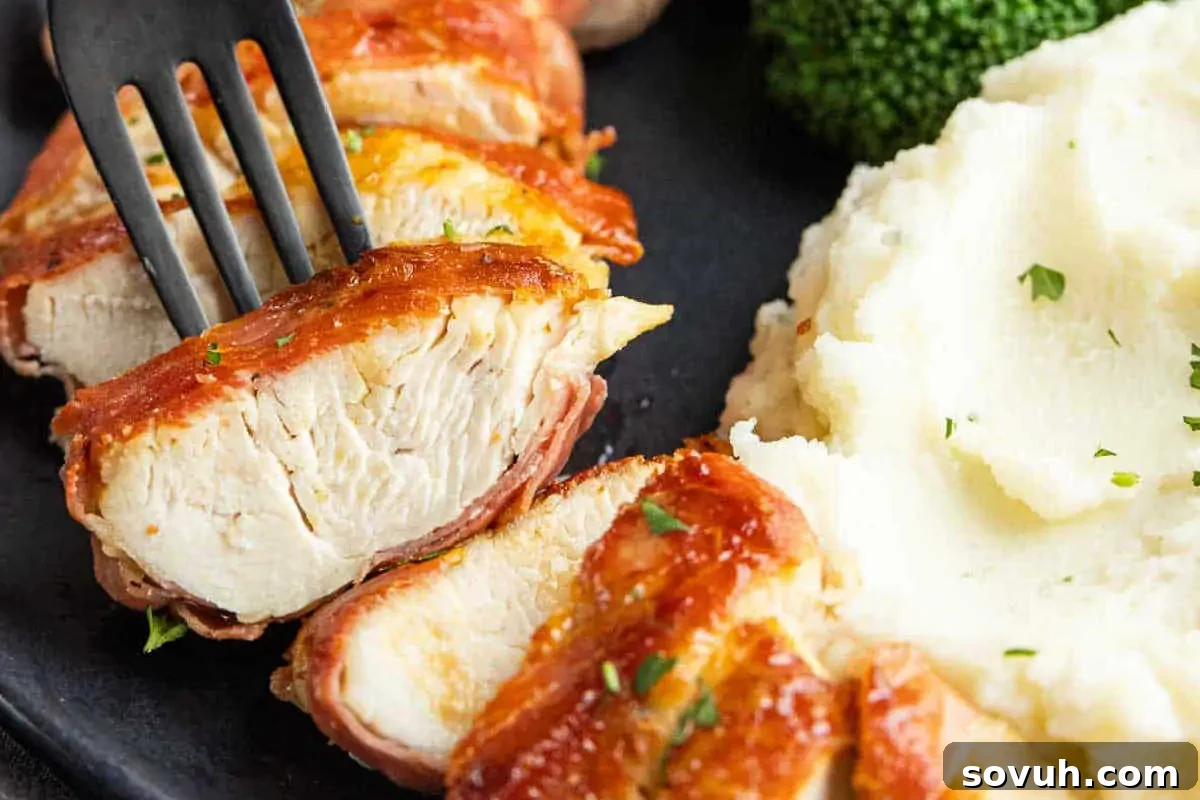 Sliced grilled chicken breast with barbecue sauce, served with mashed potatoes and broccoli on a black plate.