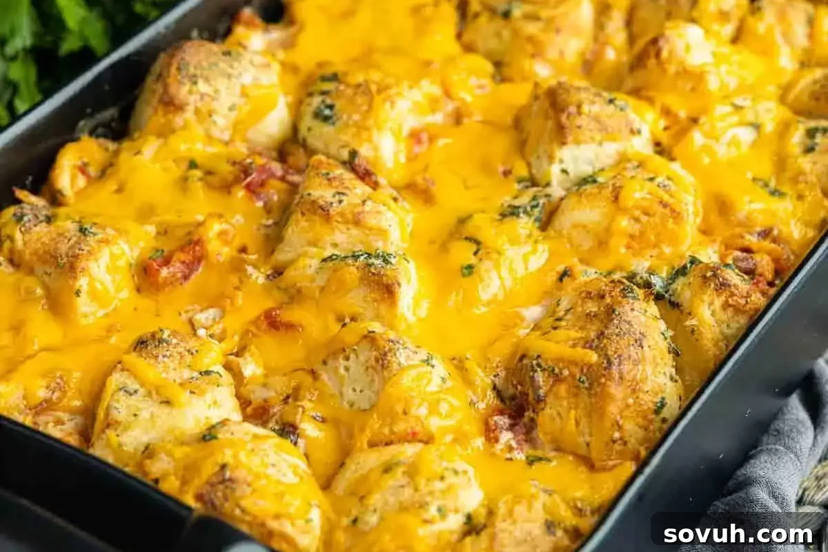 A tray of baked chicken pieces smothered in melted cheddar cheese and herbs.