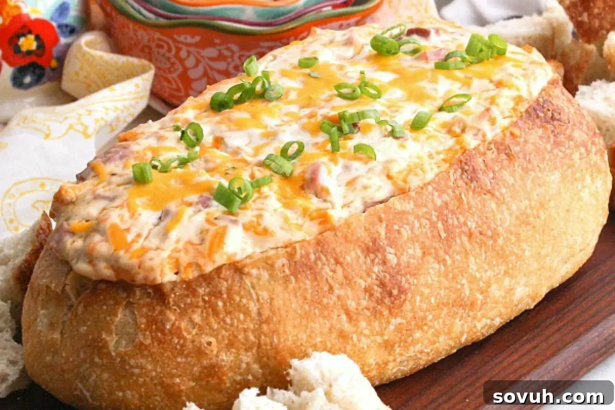 A bread bowl filled with creamy dip, topped with melted cheese and green onions, served on a wooden board.