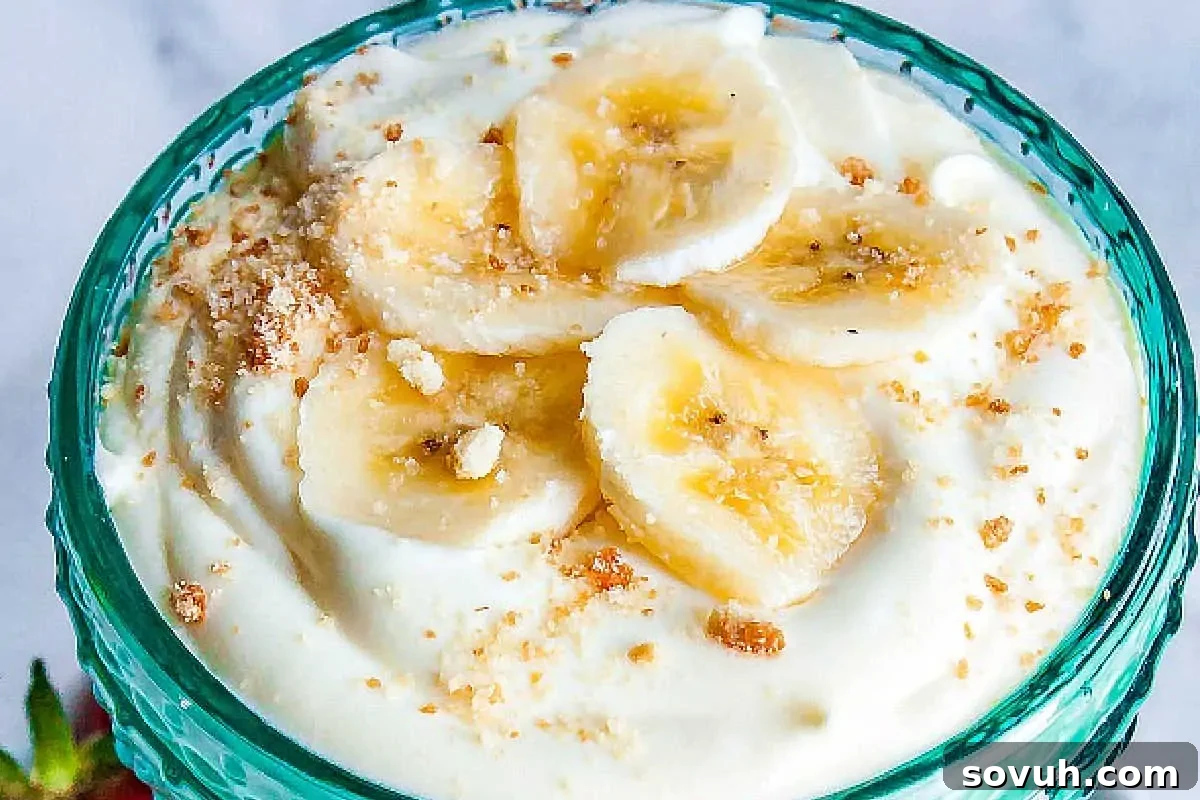 A bowl of yogurt topped with sliced bananas and crushed biscuits.