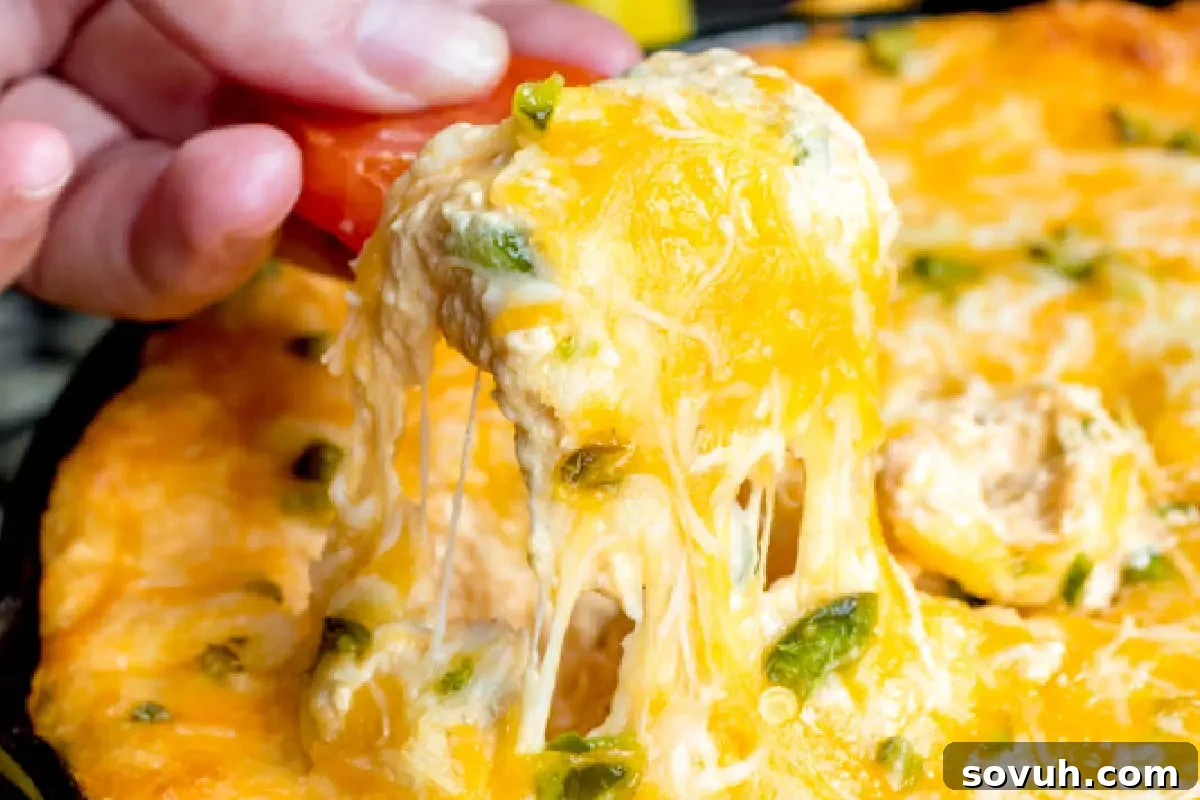 A person's hand adds a cherry tomato to a cheesy, melted slice of pizza with visible strands of cheese.