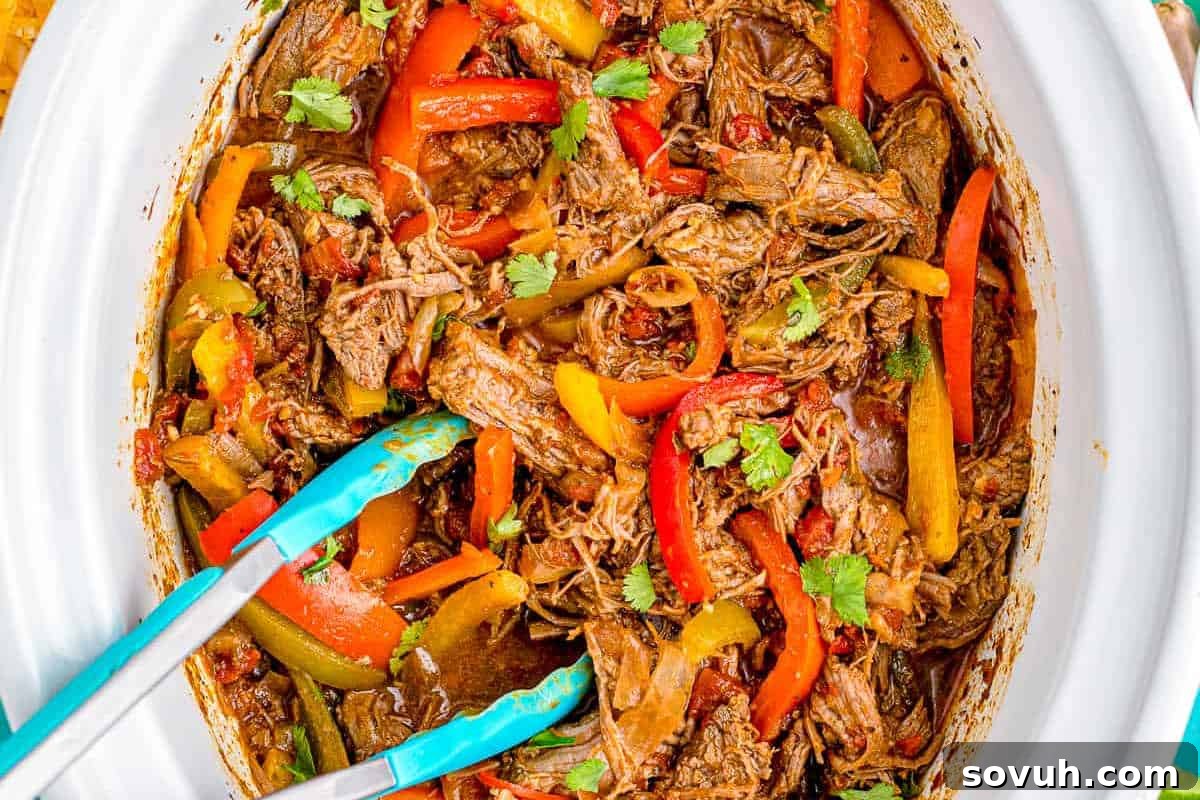 Shredded chicken with sliced bell peppers and cilantro in a slow cooker, accompanied by blue tongs.