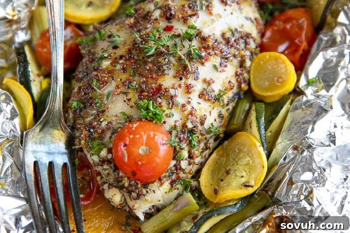 A perfectly grilled chicken breast, seasoned with fresh herbs and served alongside quinoa, cherry tomatoes, and thinly sliced zucchini and squash, all neatly presented on aluminum foil with a fork.