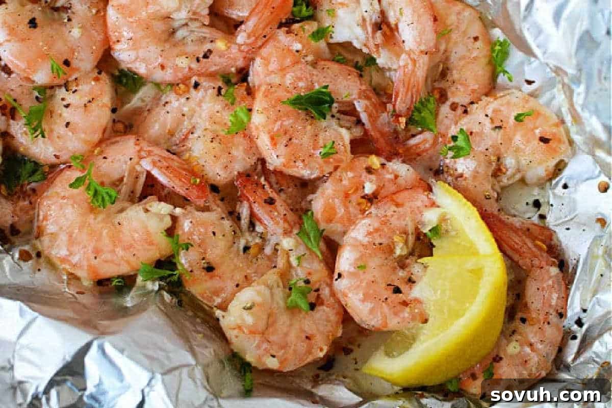 A close-up of perfectly seasoned and cooked shrimp, elegantly garnished with fresh parsley and bright lemon wedges, presented on a foil surface, ready to be enjoyed.