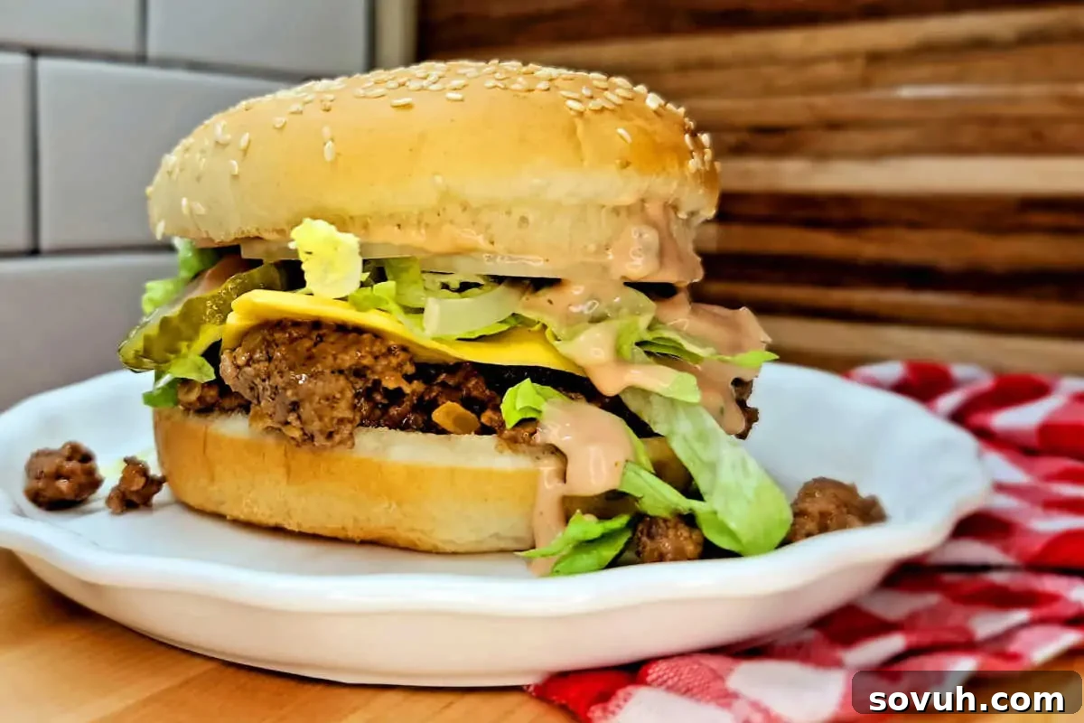 A cheeseburger with lettuce, onions, and sauce on a sesame seed bun, served on a white plate with a red and white checkered napkin.