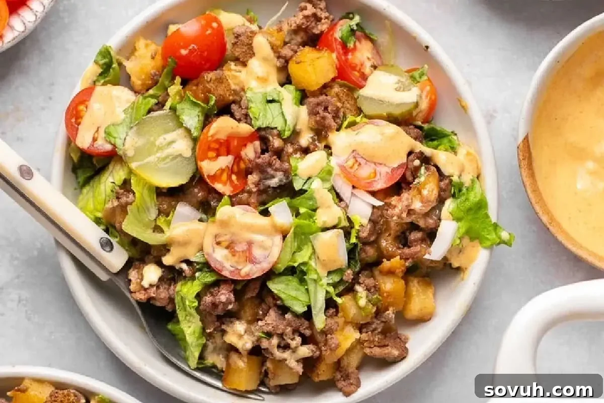 A bowl of taco salad with ground beef, lettuce, tomatoes, onions, and a creamy dressing, served in a white dish.