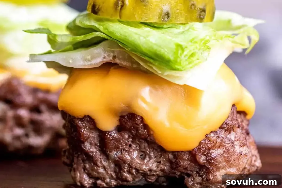 Close-up of a burger with melted cheese, lettuce, and pickles on a beef patty, presented as a bite-sized appetizer.