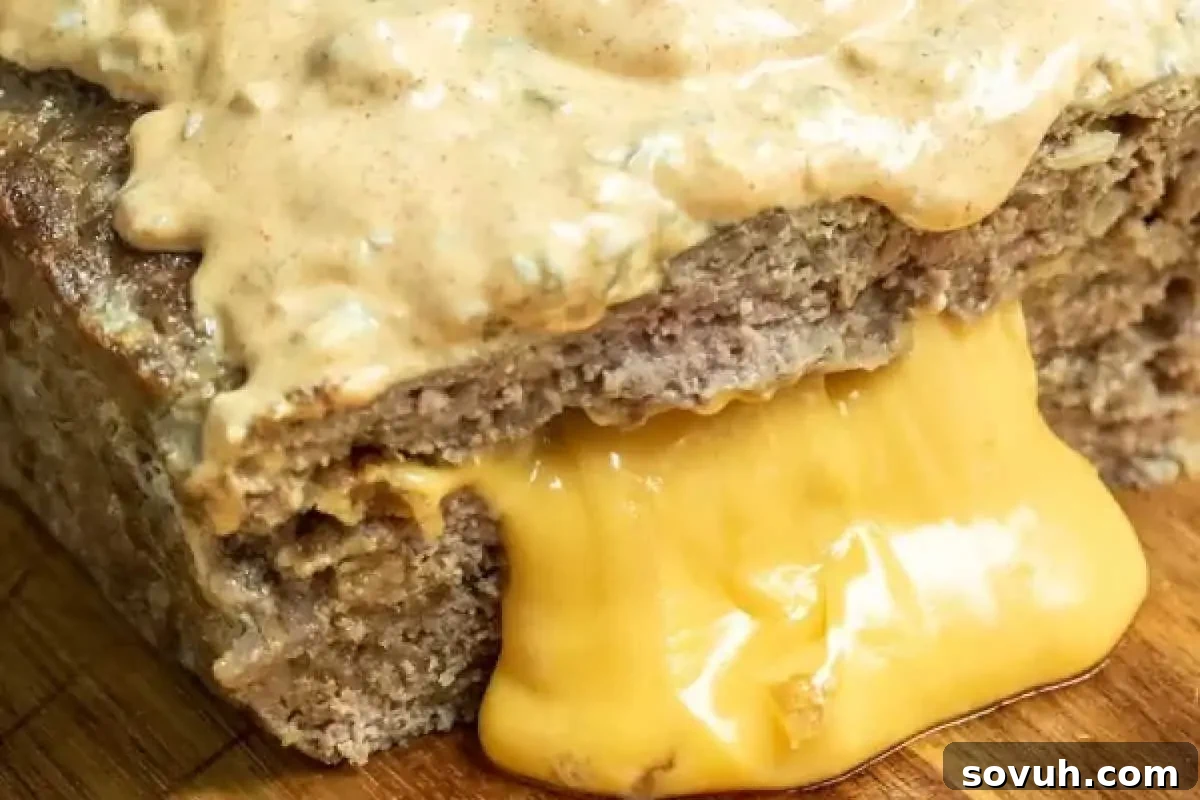 A close-up of a meatloaf slice topped with creamy sauce, featuring melted cheddar cheese oozing down the sides.