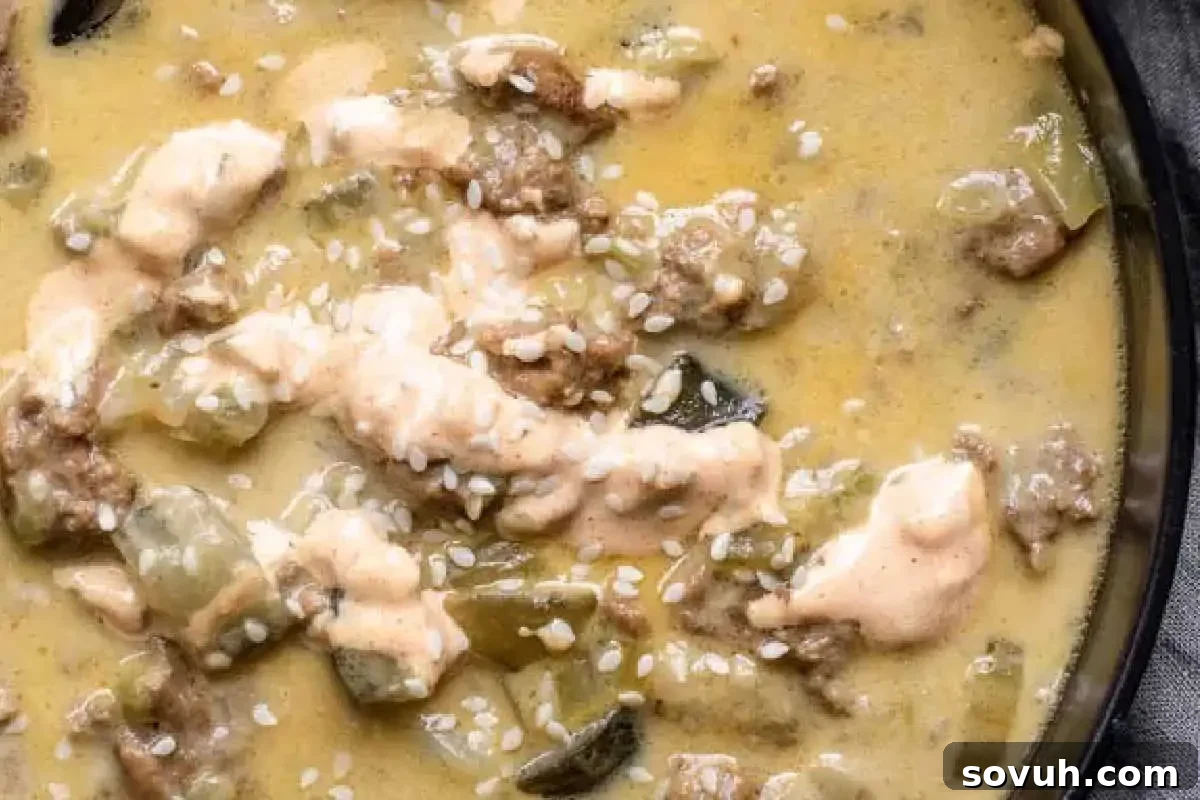 Close-up image of a creamy soup garnished with sesame seeds, featuring chunks of chicken and sliced green peppers in a black bowl.