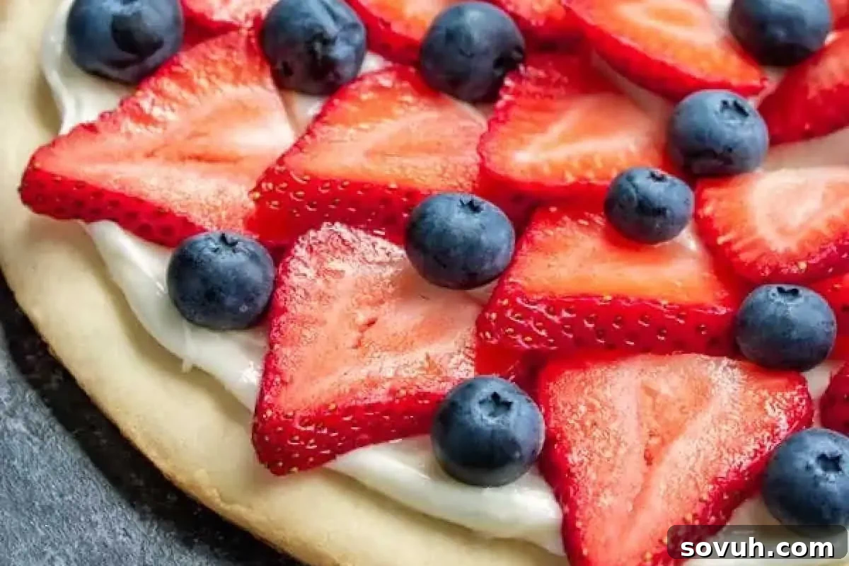 A close-up of a dessert pizza topped with a layer of cream, fresh strawberry slices, and whole blueberries.
