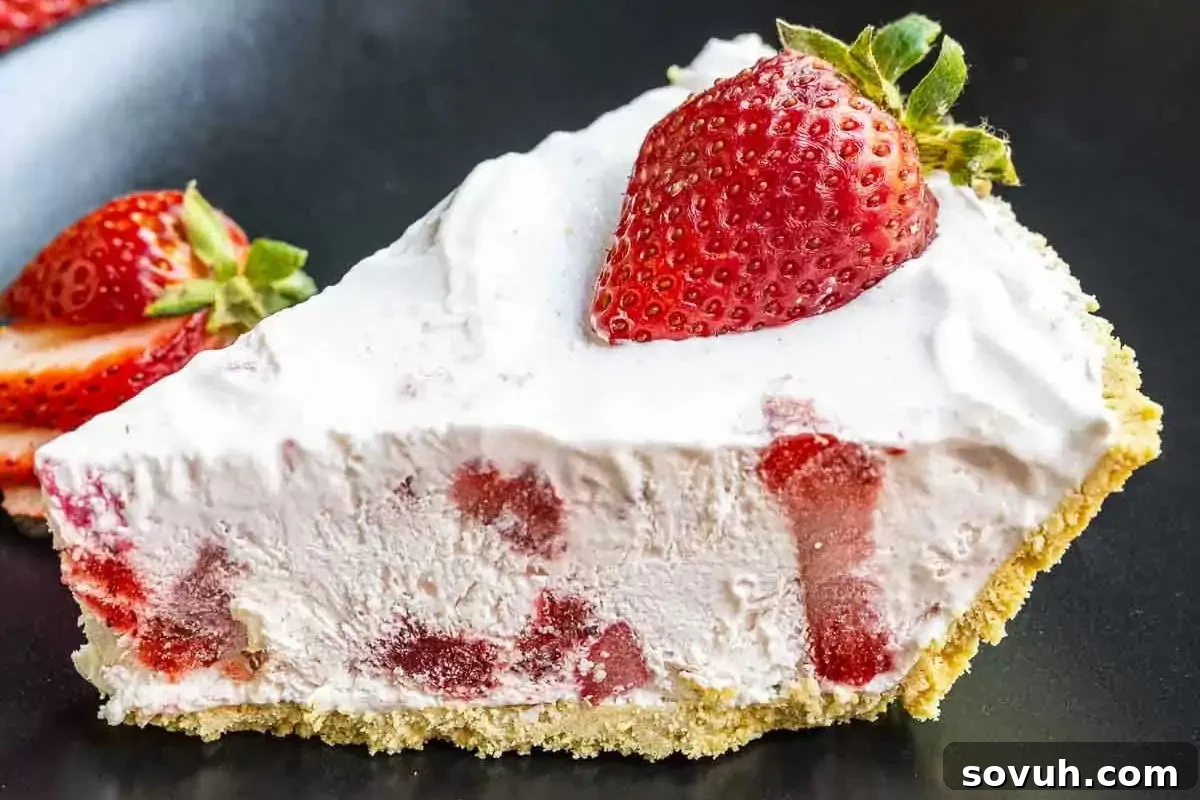 A slice of strawberry cream pie with a crumbly crust, topped with a fresh whole strawberry, displayed on a black plate.