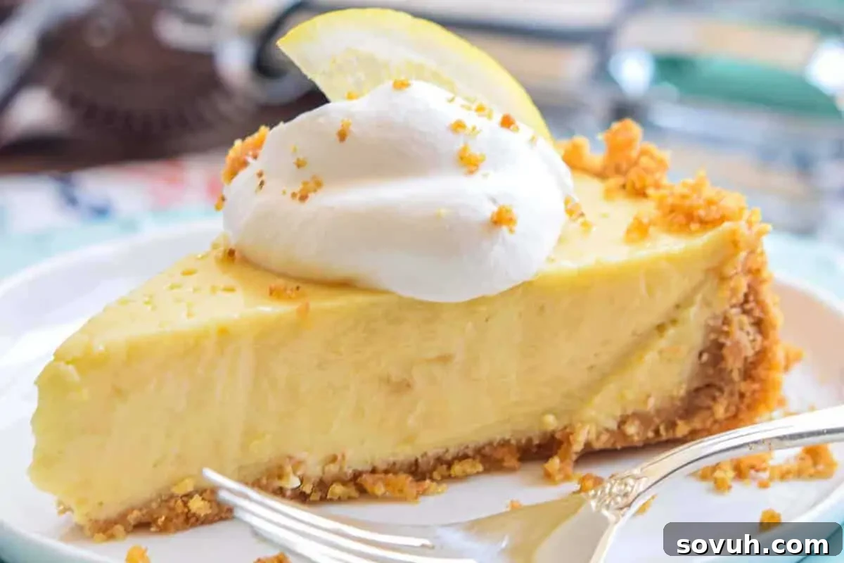 A slice of creamy lemon pie topped with a dollop of whipped cream and a lemon slice, served on a white plate with a fork beside it.