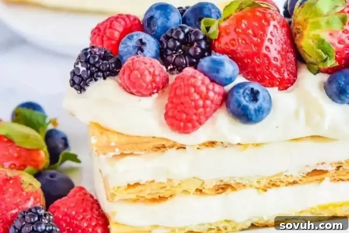A layered dessert topped with cream and an assortment of fresh berries including strawberries, raspberries, blackberries, and blueberries.