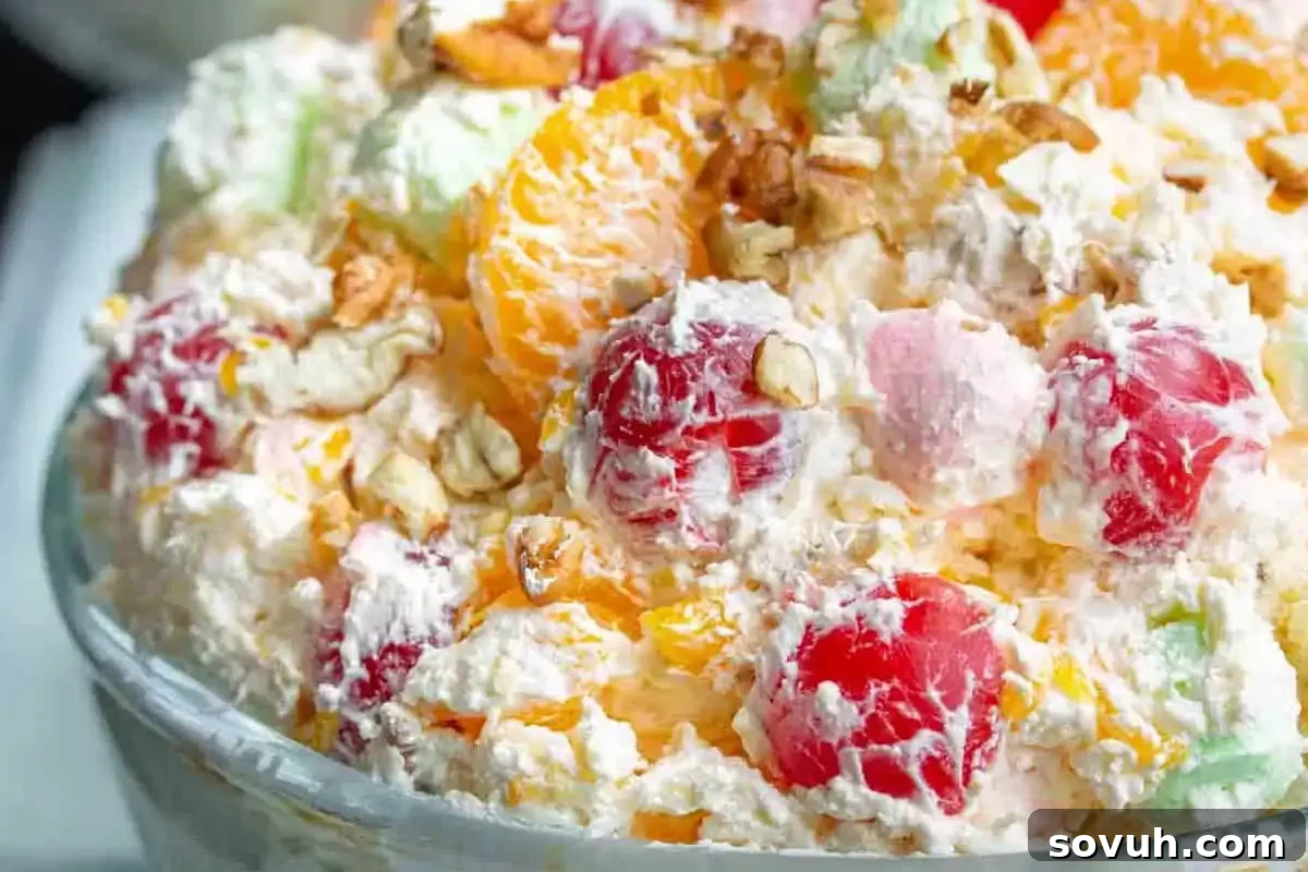 A close-up of a bowl filled with a colorful fruit salad, including cherries, mandarin oranges, marshmallows, and nuts, all mixed with a creamy, fluffy mixture.