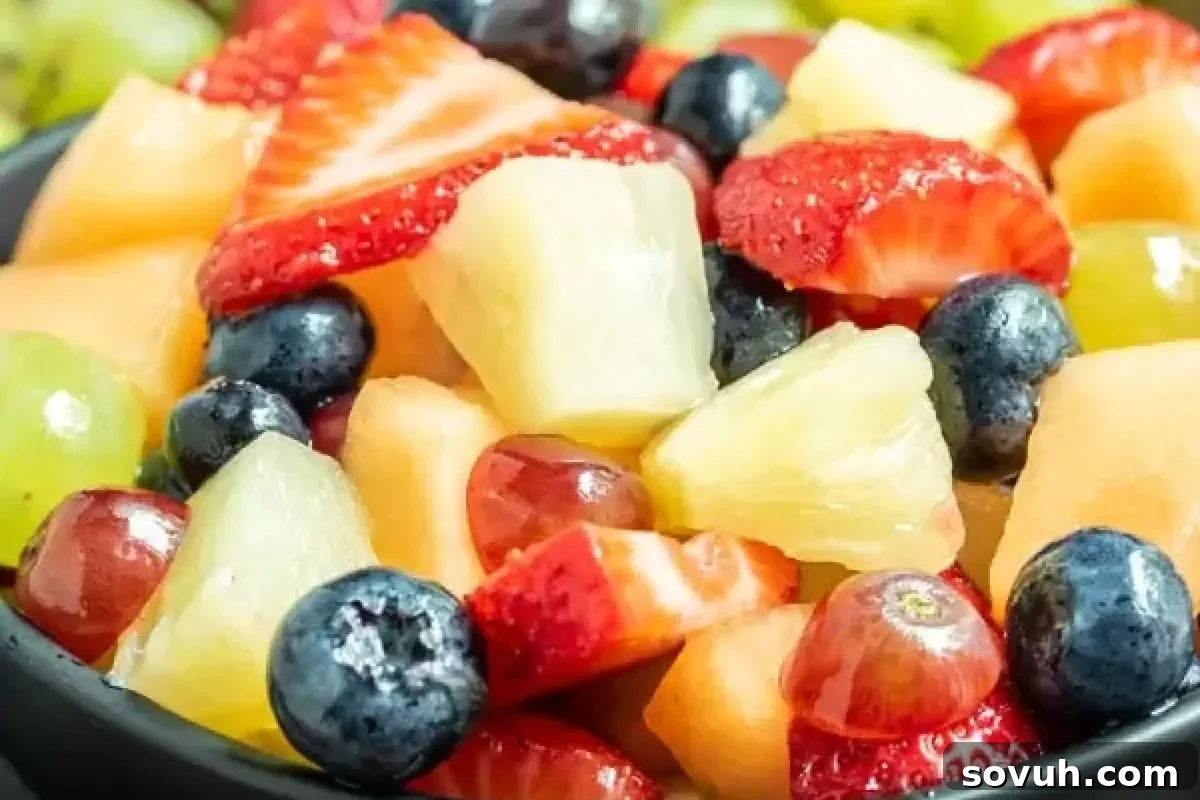 A bowl containing a mixture of assorted fresh fruit, including strawberries, blueberries, grapes, pineapple, and melon pieces.