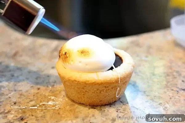 A brulee torch being used to toast marshmallows on S'mores Cookie Cups.