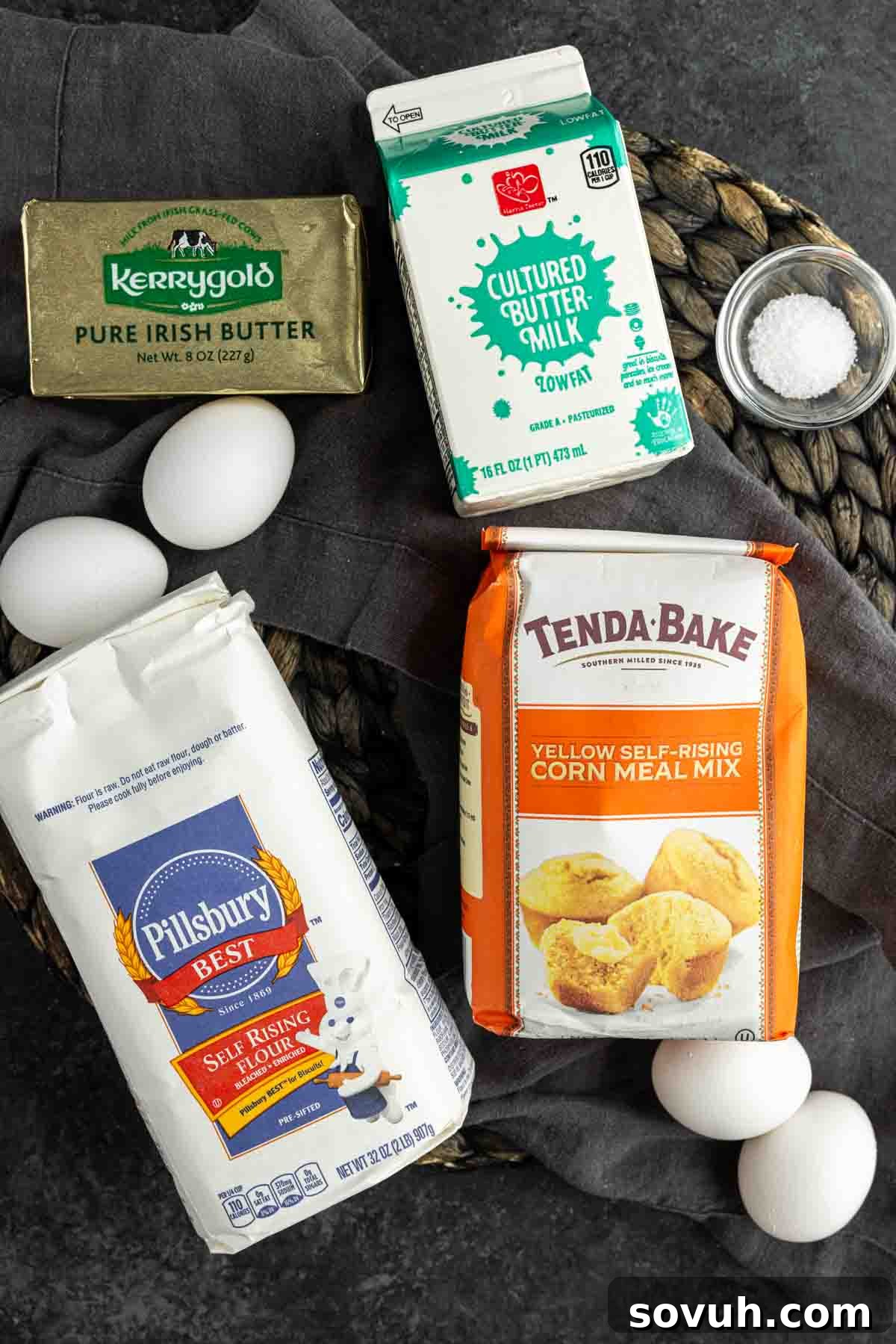 Ingredients for baking Southern Cornbread Recipe laid out on a surface: Kerrygold butter, cultured buttermilk carton, a bowl of salt, fresh eggs, a bag of Pillsbury self-rising flour, and a bag of Tenda-Bake cornmeal mix.