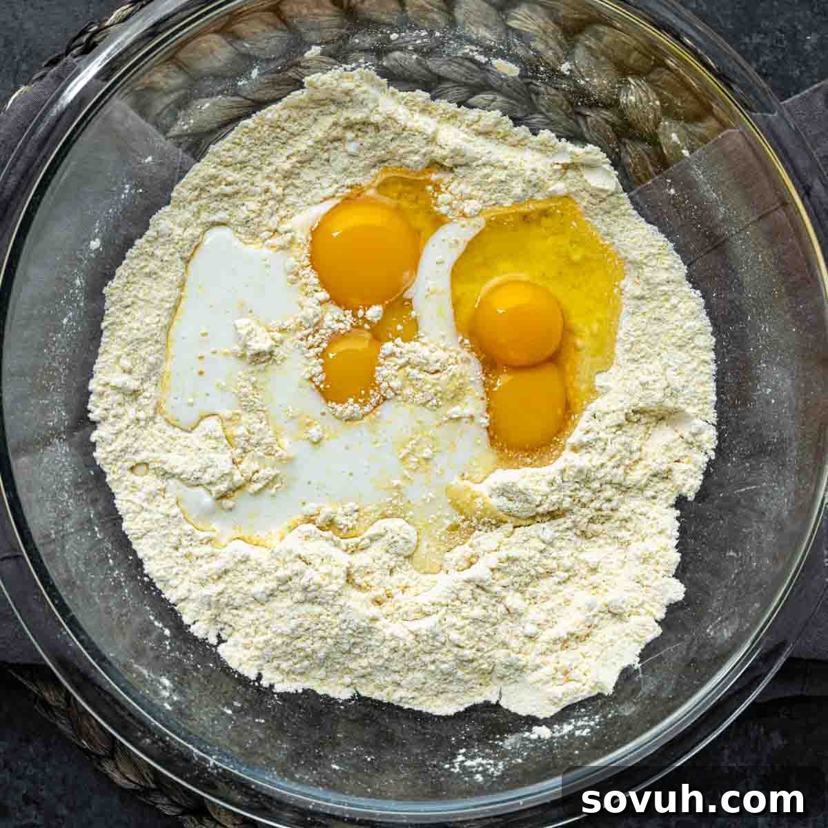 A mixing bowl containing self-rising flour, two cracked eggs, buttermilk, and vegetable oil, ready to be combined for baking a delicious Southern Cornbread Recipe.