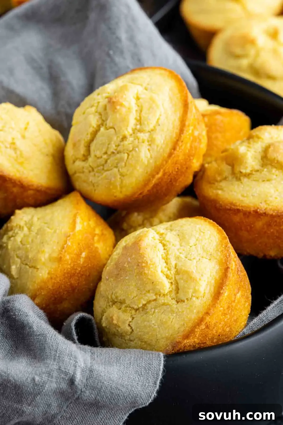 A bowl filled with freshly baked Southern Cornbread muffins, some resting on a gray cloth. The muffins have golden-brown tops and a slightly crumbly texture, ready to be enjoyed.