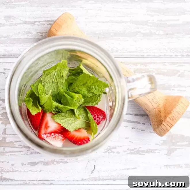 A glass jar with strawberries and mint in it.