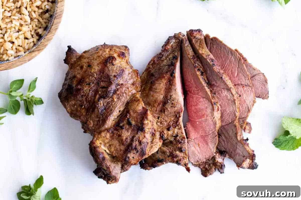 Grilled and sliced lamb with a side of rice, garnished with fresh herbs, displayed on a white surface.